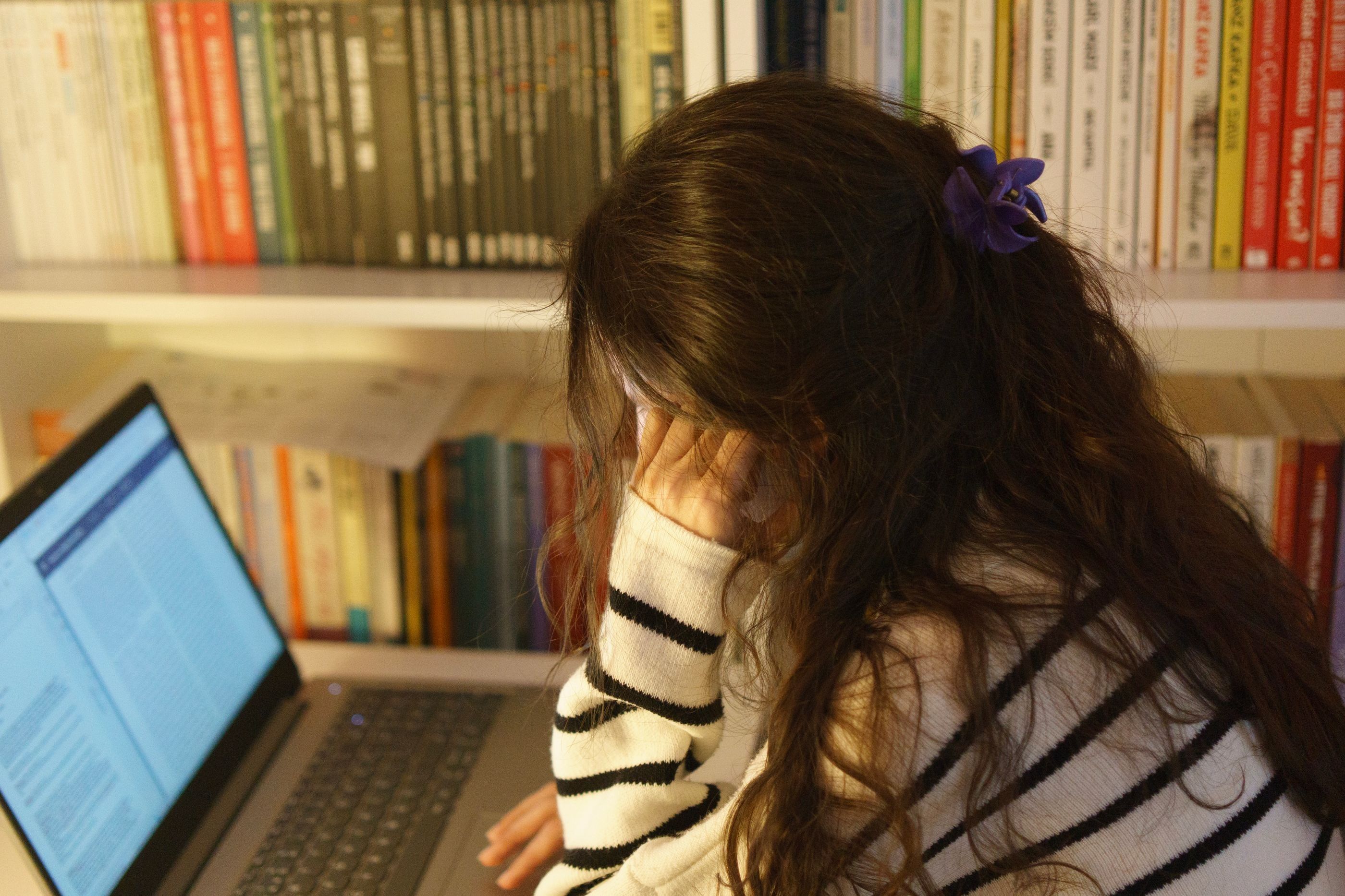 Uczennica przy laptopie na tle regału z książkami